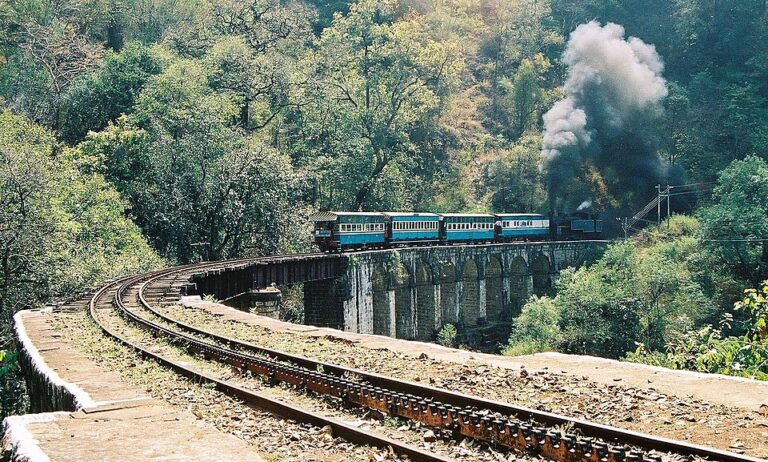 Nilgiri Mountain Railway toy train crossing a tall viaduct bridge amidst lush green hills near Ooty, India